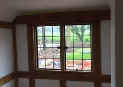 Interior corner with a wooden‑framed heritage metal‑style window featuring black grid handles, set within white walls and exposed timber detailing, overlooking a grassy outdoor area.