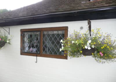 White‑brick exterior with a dark timber‑framed diamond‑paned heritage metal‑style window, framed by colourful hanging flower baskets.