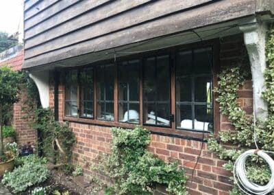 Row of black metal‑framed heritage windows set into a brick and timber exterior with climbing greenery.