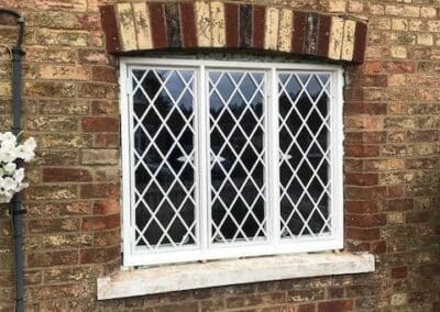 Heritage‑style metal lattice window with diamond glazing set into a traditional brick wall with an arched header.