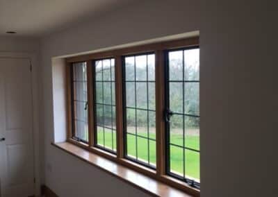 Interior room with a four‑pane wooden‑framed heritage metal‑style window featuring black grid bars and opening handles, overlooking a grassy outdoor area.
