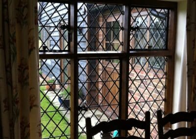 Interior dining nook looking out through a diamond‑paned heritage metal‑style window onto a traditional garden.