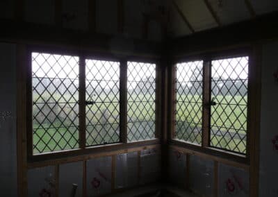 Diamond‑pattern heritage metal windows installed in a room under renovation, surrounded by insulation panels.
