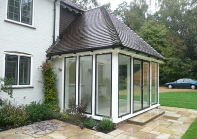 Modern white brick house with a black‑framed glass conservatory extension overlooking a garden.