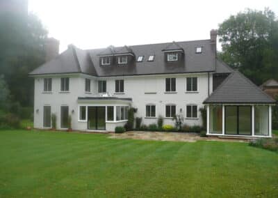 Large white two‑storey house with dormer metal windows, grey tiled roof and a landscaped garden.