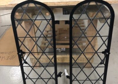 Arched black metal window panels with diamond-pattern glazing leaning against a pallet in a workshop.