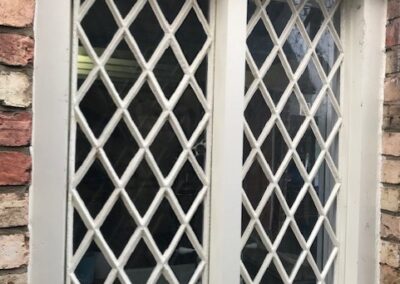White metal lattice window with diamond-pattern glazing set into a rustic brick wall.