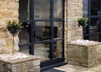 Arched black metal windows and doors installed in a stone property with modern planters.