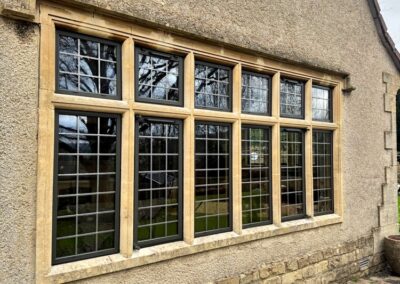 Large multi‑pane window with black grid muntins set in a beige stone surround on a traditional exterior wall.