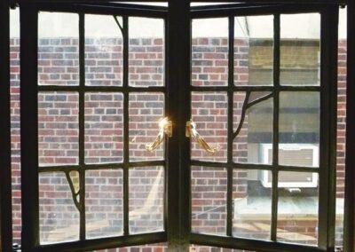 Close‑up of a multi‑pane metal‑style window with reflective handles and a brick exterior view.